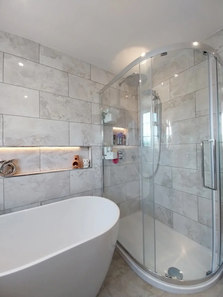 A luxurious steam shower setup featuring a sleek glass enclosure with a curved door, a modern overhead showerhead, and a handheld shower, complemented by a white bathtub, stylish tile walls, and recessed lighting with decorative shelves.