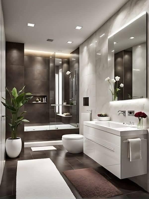 A modern bathroom in our service areas, featuring a sleek glass shower, white vanity with mirror, freestanding tub, and stylish decor with plants and flowers.