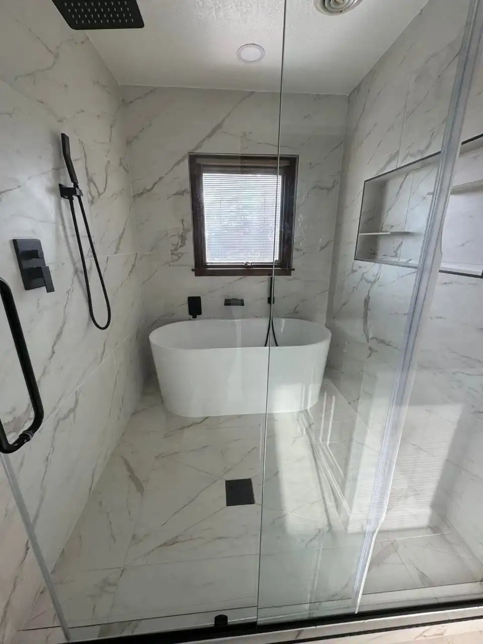 A stunning luxury shower and tub combo with a sleek glass enclosure, black fixtures, a modern freestanding tub, and elegant marble tiles, enhanced by natural light.
