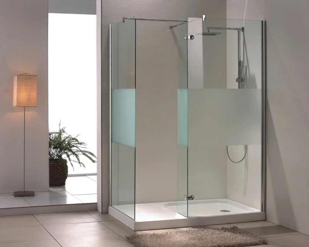 A modern walk-in shower installation with clear glass panels, a frosted privacy section, and a sleek overhead showerhead, complemented by a white tray base, set in a minimalist bathroom with a potted plant and soft lighting.